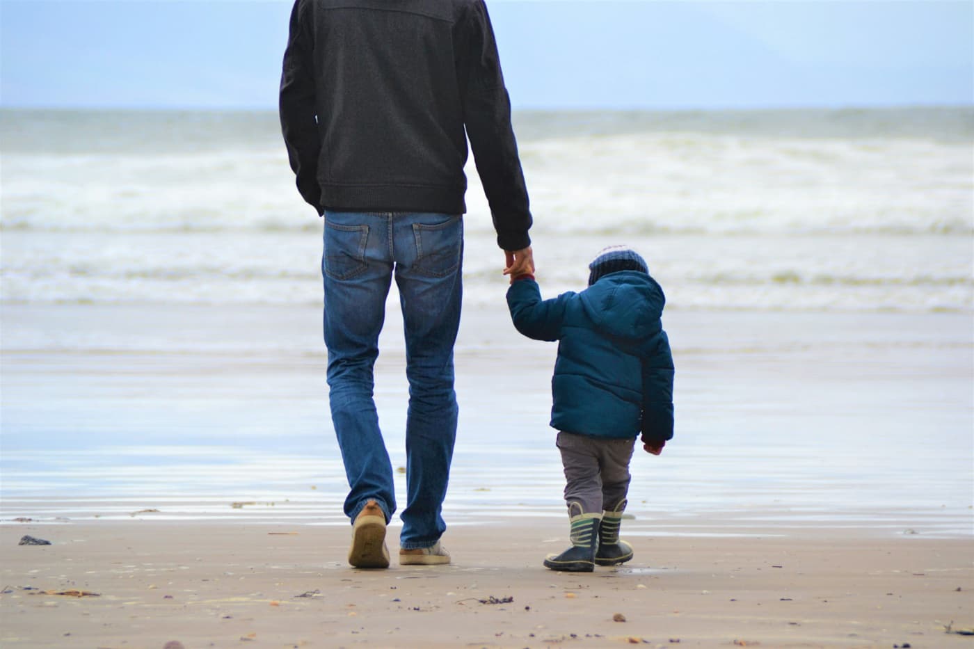 Un padre y su hijo pequeño caminando de la mano por la playa